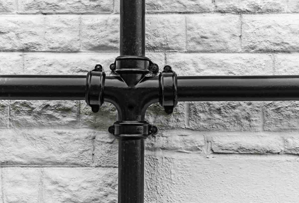 Black cast iron LCC soil pipe stack with a cross branch and eared sockets fixed to a painted brick wall