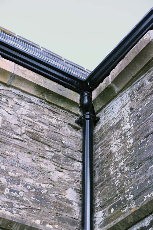 Black cast iron gutter and downpipe at the corner of a stone church in South Petherwin, Cornwall