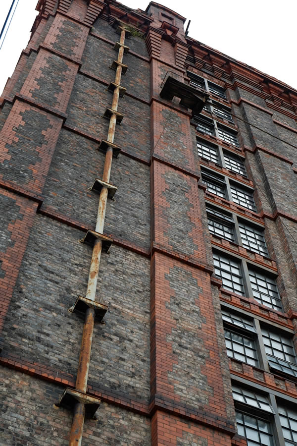 Multi-storey brick and stone mill building with cast iron rainwater pipes and iron-framed windows