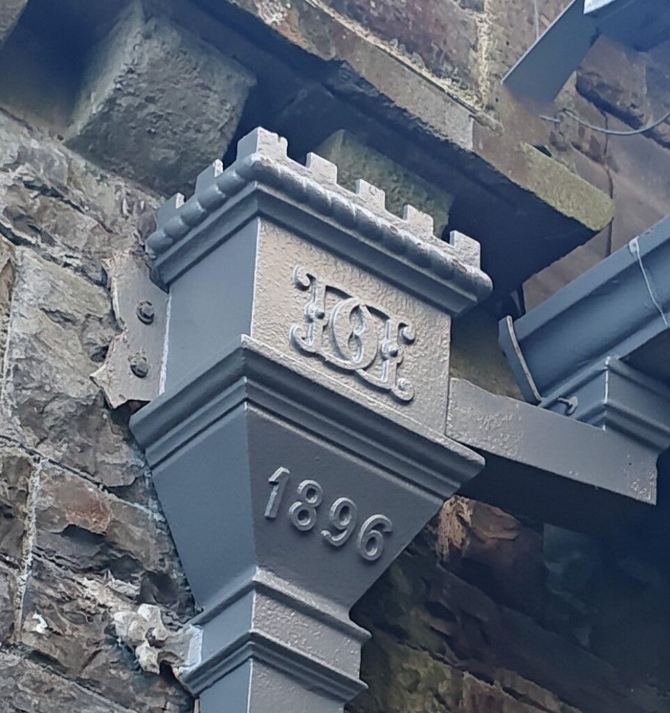 Dated cast iron hopper head with a raised monogram fixed to a stone wall