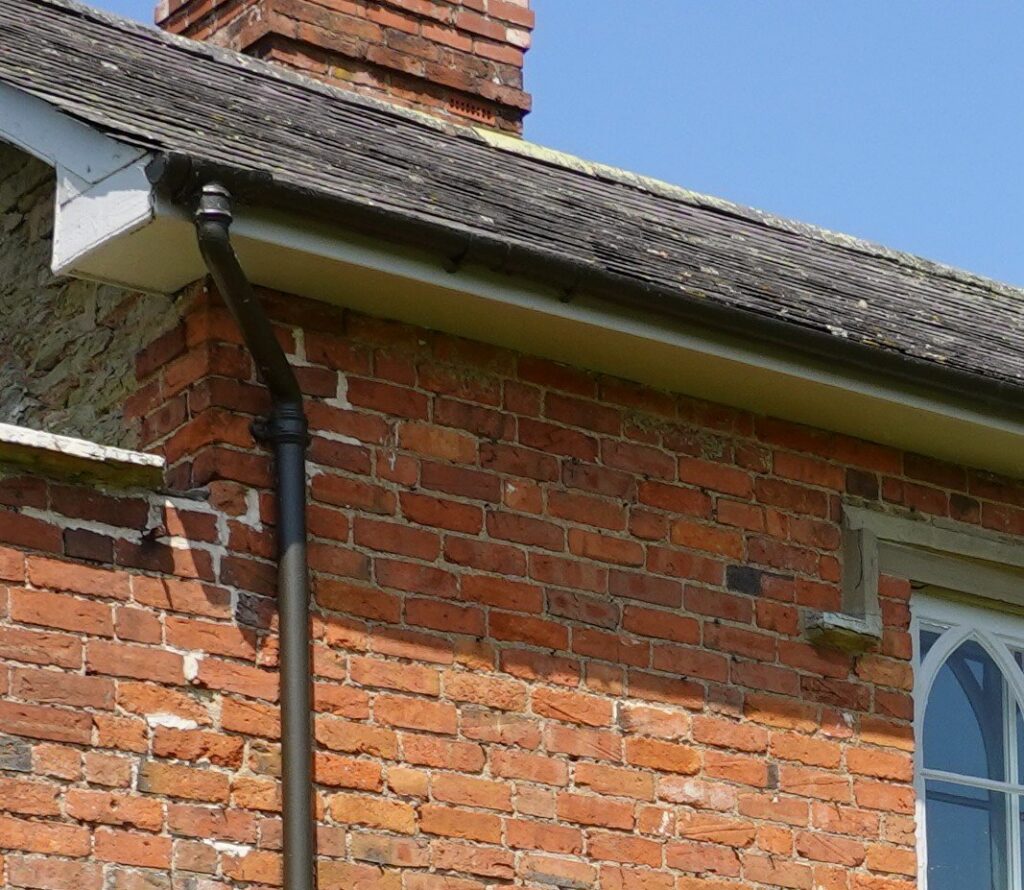 Round cast iron downpipe with eared socket joints on a red brick wall