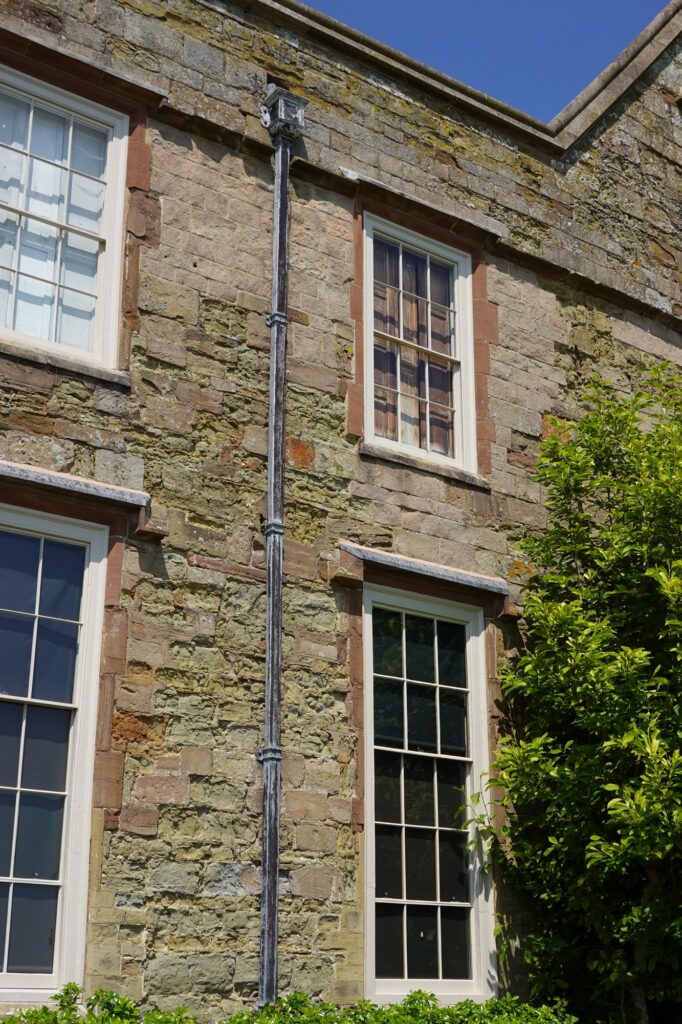 Cast iron downpipe running down a stone elevation beside a sash window