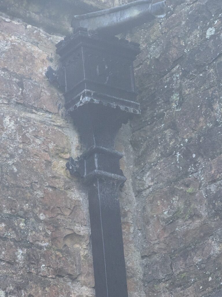 Cast iron box gutter outlet on a stone church wall, Magor