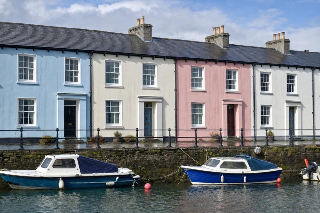 Black cast iron ogee gutter and round downpipes along a colour-washed Regency terrace with Welsh slate roofs in a Ceredigion harbour town.
