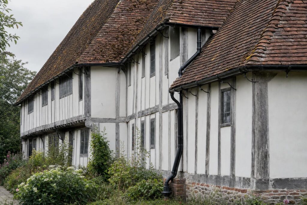 Black-painted cast iron beaded half-round gutter and round downpipe on a jettied Wealden hall house with peg-tile roof in the Kent Weald.