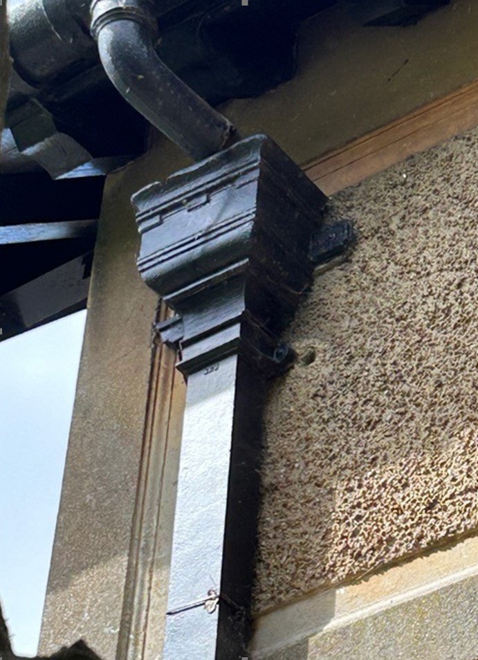 Rectangular cast iron hopper head with a castellated top edge, installed