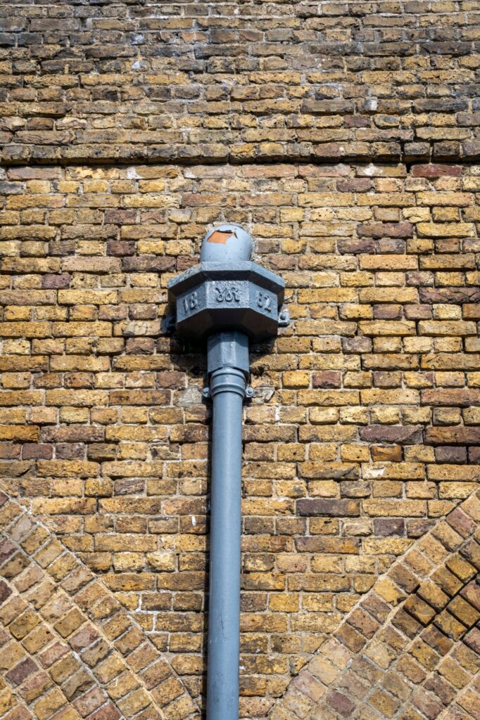 Cast iron hopper head with a cast date plate, on a yellow brick wall