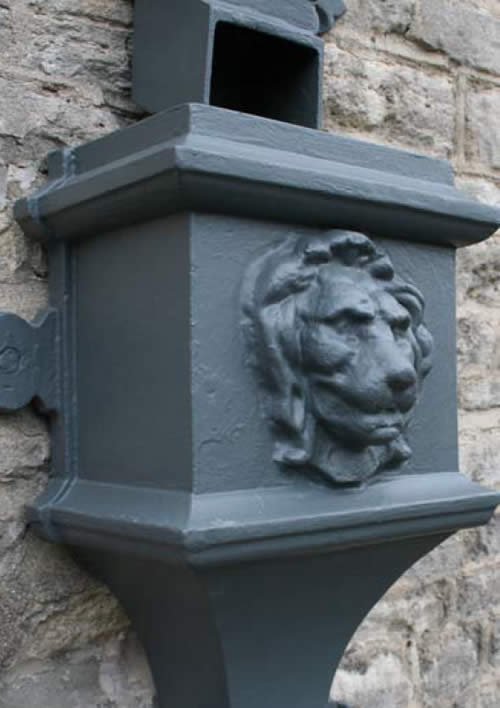 Cast iron hopper head with a cast lion's head motif, installed on a stone building