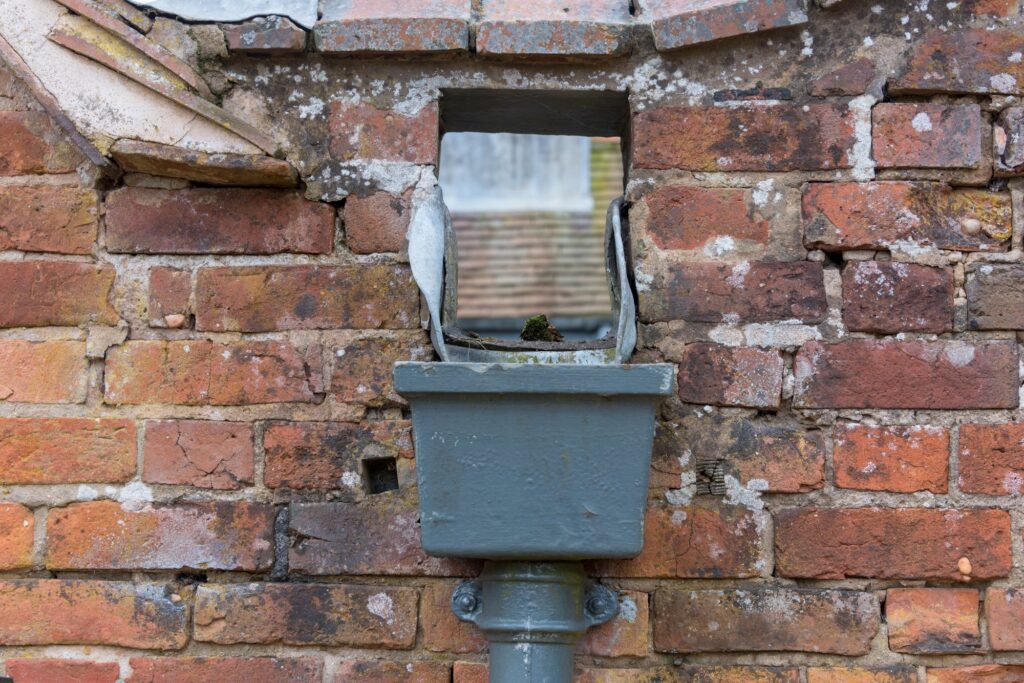 Weathered cast iron square hopper head on a red brick wall
