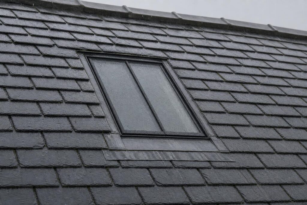 Slim black steel conservation rooflight with single central glazing bar, rain sheeting across the glass on a slate roof