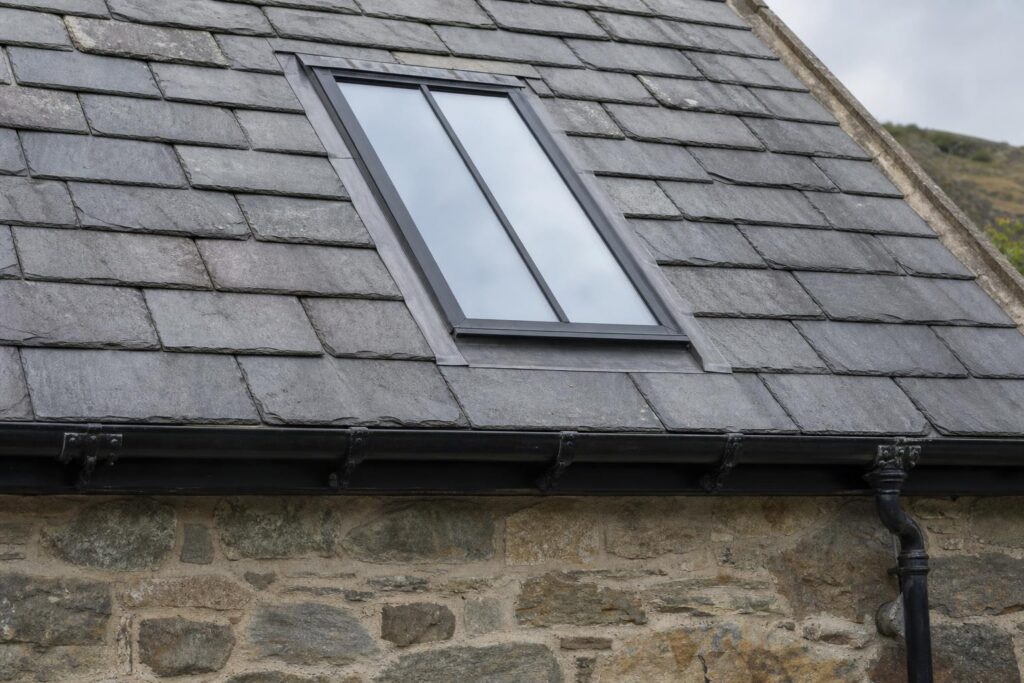 Slim black steel conservation rooflight with a central glazing bar set flush in a Welsh slate roof above a black cast iron gutter
