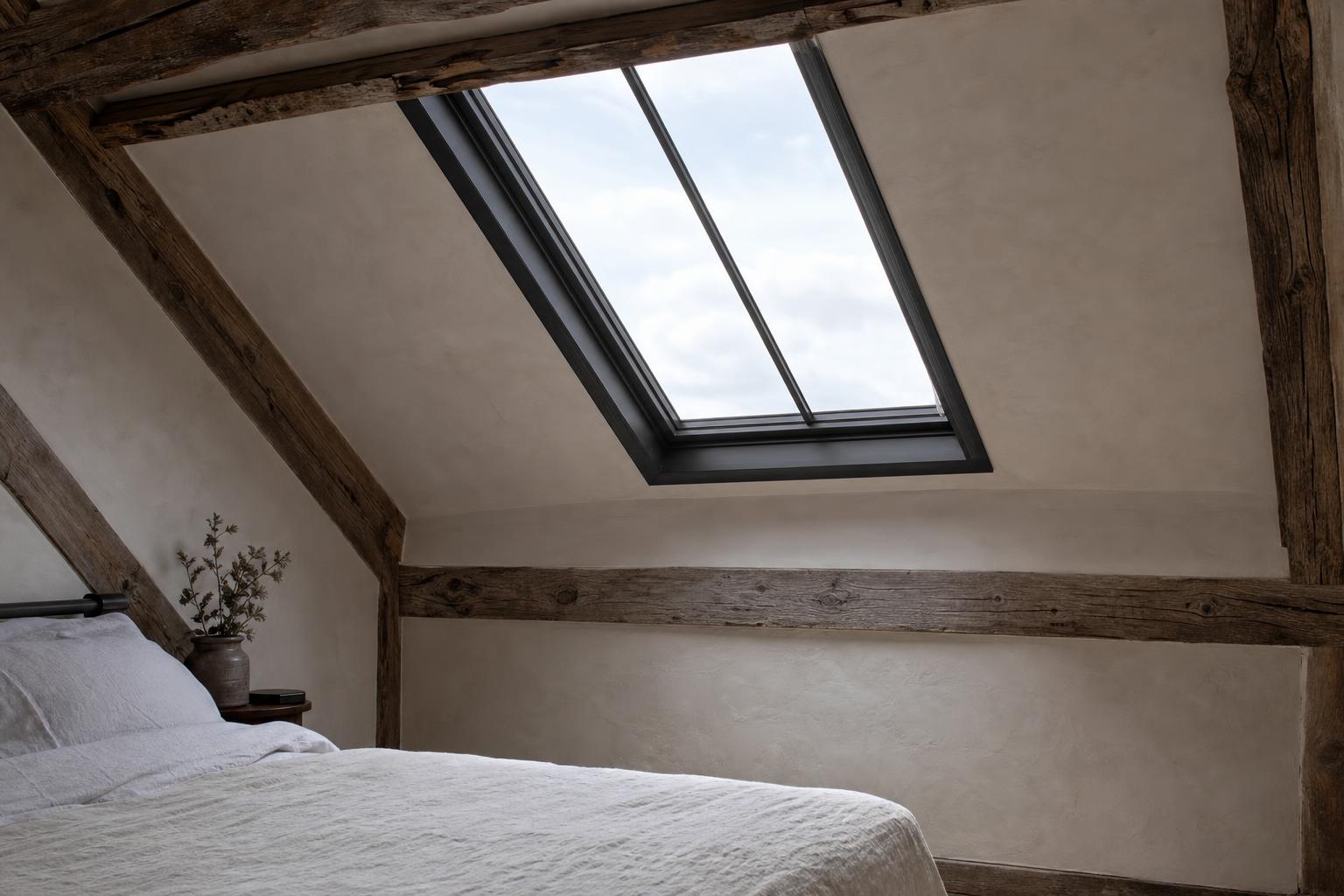 Attic bedroom lit by a conservation rooflight in a sloping plastered ceiling between old oak timbers