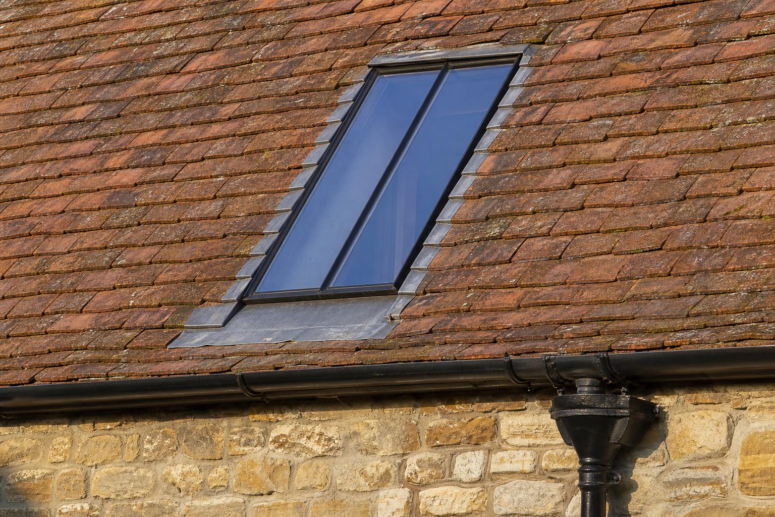 Lead flashings around a flush black steel rooflight in a clay tile roof, with a cast iron gutter and hopper head below