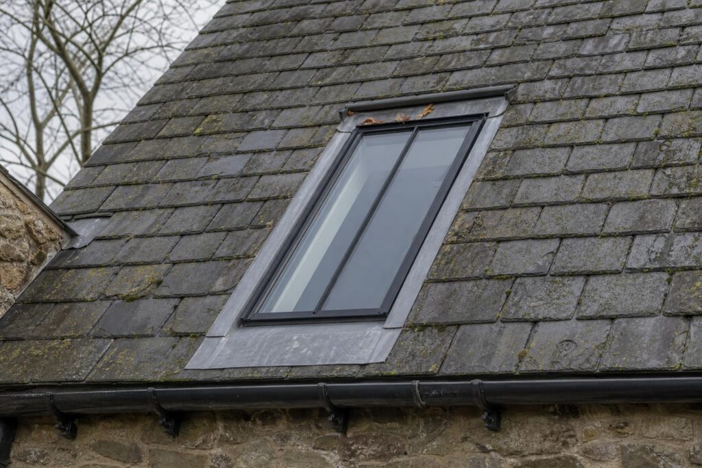 Slim black steel conservation rooflight set flush in a slate roof with lead flashings and a black cast iron half-round gutter at the eaves