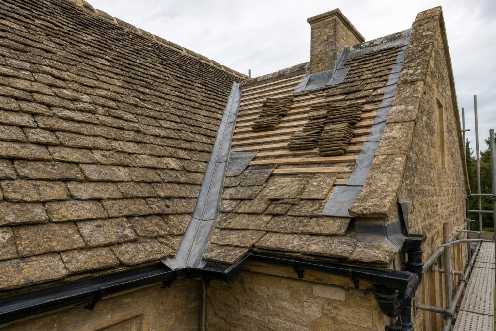 Cotswold stone slate roof in diminishing courses with a lead-lined valley, a stripped section on battens and a cast iron gutter