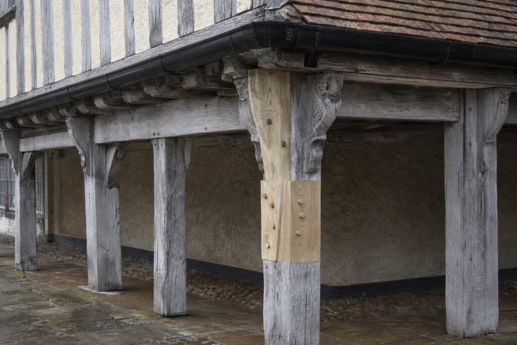 Jettied timber-framed house with lime-rendered panels and a new pegged oak scarf repair in a ground-floor post