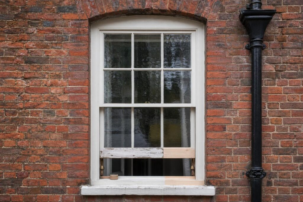 Georgian six-over-six timber sash window under repair with a new spliced timber section at the sill and rippled crown glass