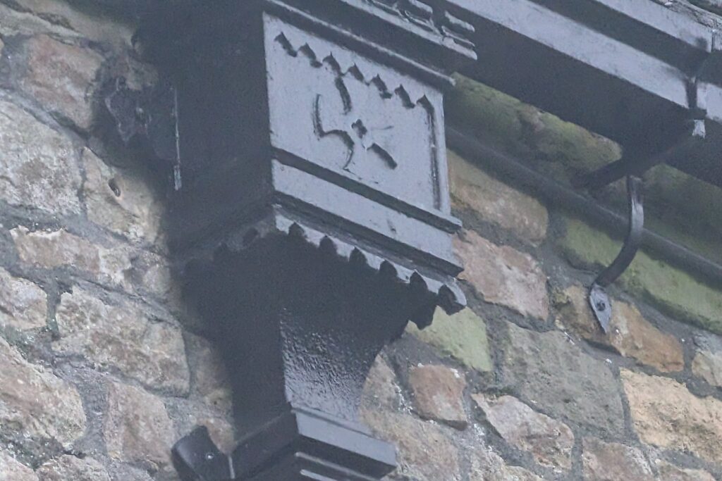 Close up of an ornamental Gothic cast iron hopper head with castellated top, foliate motif and dentil base on a rubble stone church wall, photographed during a site survey
