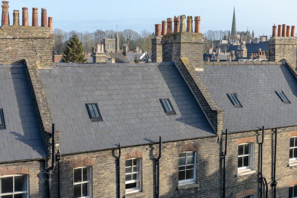 Slate roofs of a conservation area terrace with small flush rooflights, chimney stacks and cast iron downpipes.