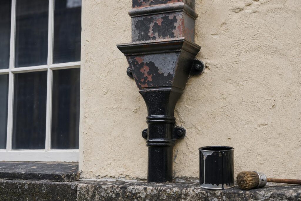 Cast iron hopper head and downpipe part-way through repainting, fresh matt black over old flaking paint and primer