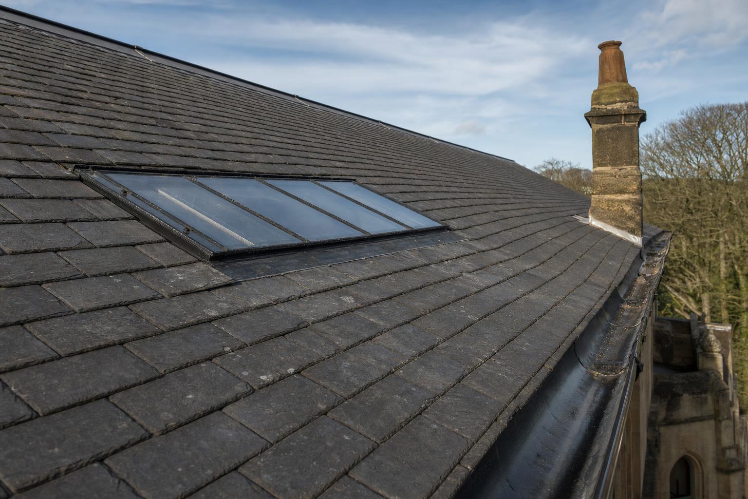 A low-profile conservation rooflight sitting within the plane of a slate roof, showing minimal projection above the slates.