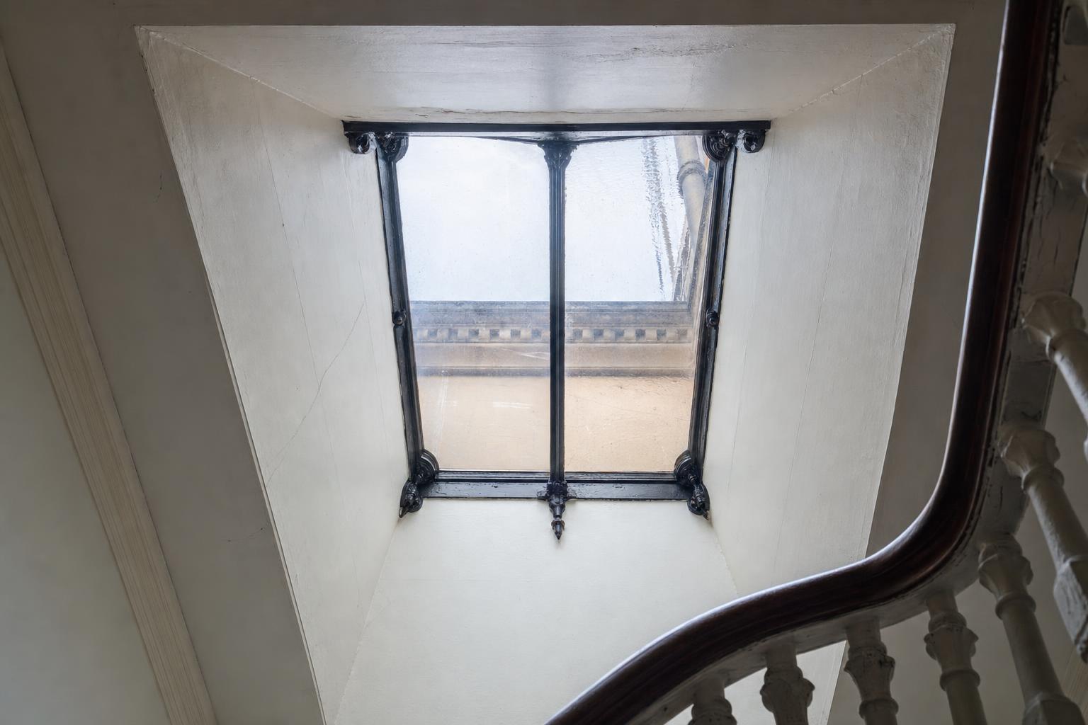 A nineteenth-century cast iron rooflight with a central glazing bar seen from inside a Victorian stairwell.