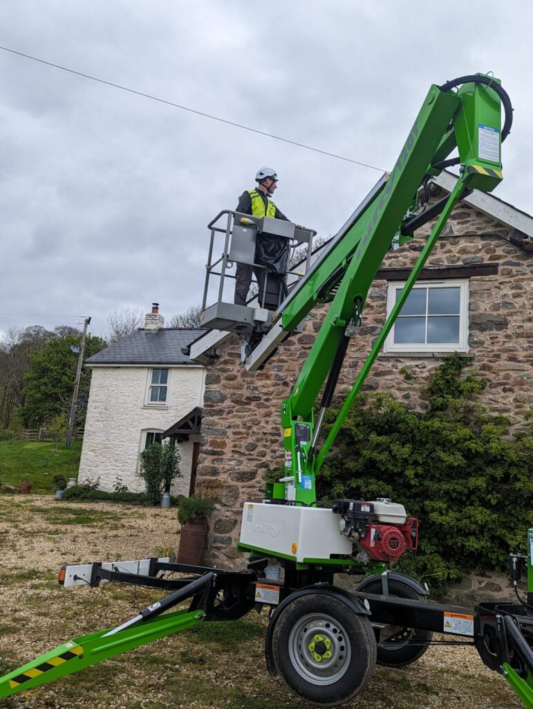 Surveyor on a tracked aerial platform inspecting the gutters of a stone cottage