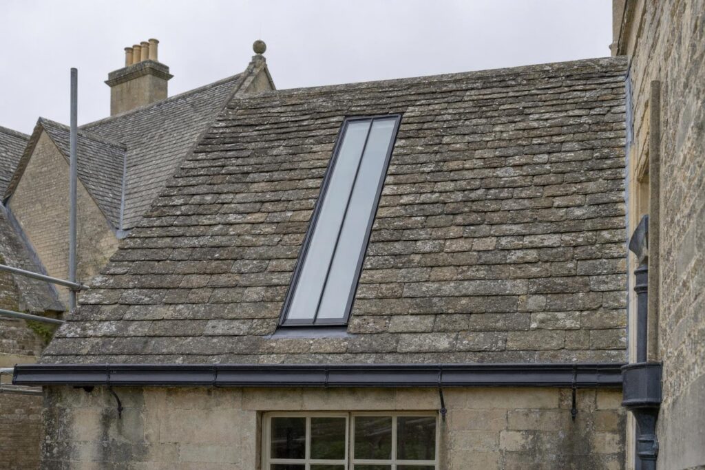 A long, narrow purpose-made conservation rooflight with a single central glazing bar set flush into the stone slate roof of a Georgian country house.
