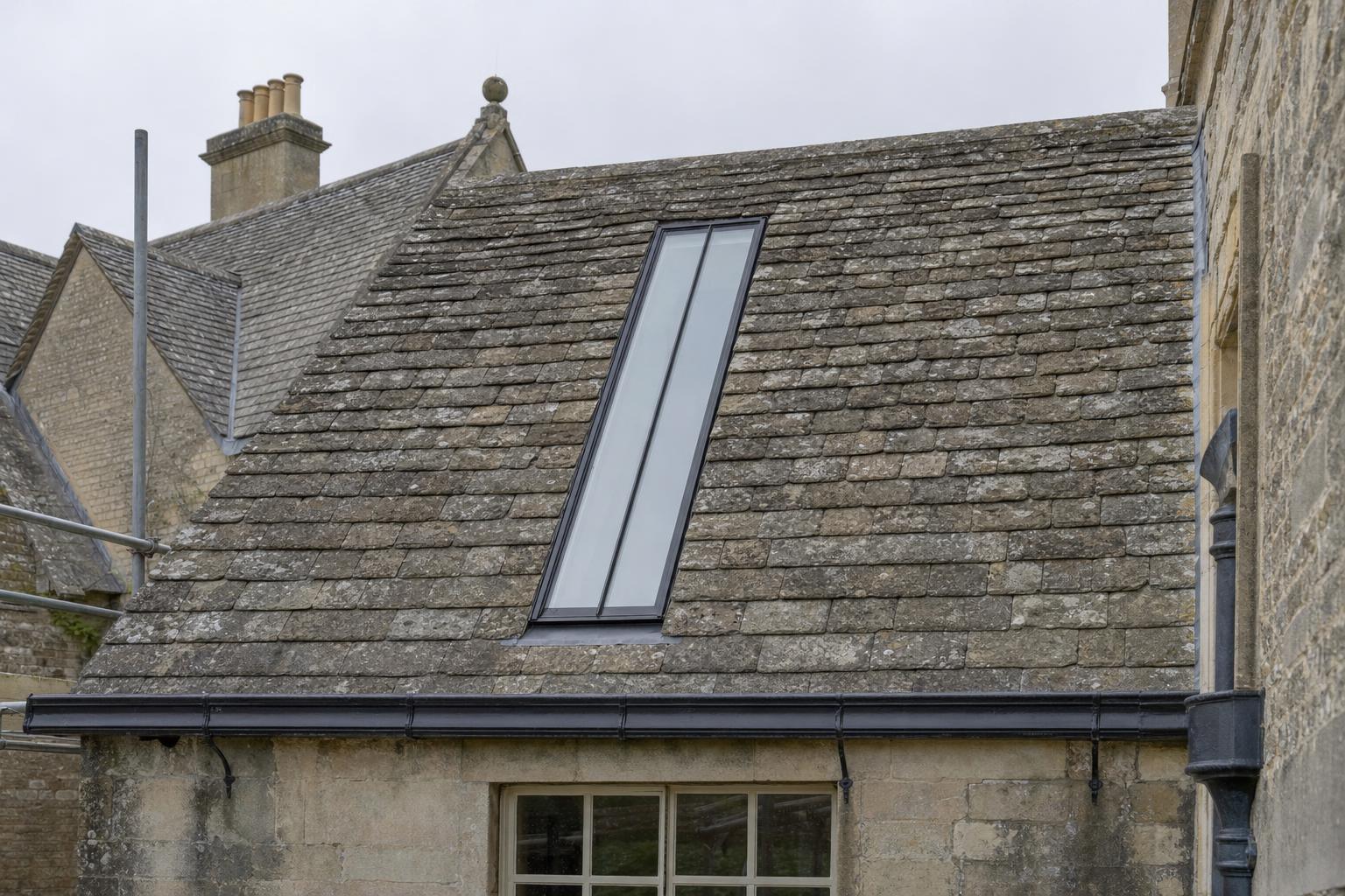 A long, narrow purpose-made conservation rooflight with a single central glazing bar set flush into the stone slate roof of a Georgian country house.