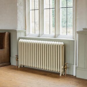 Board School two-column cast iron radiator with rounded tops beneath a tall window in a Victorian village hall.