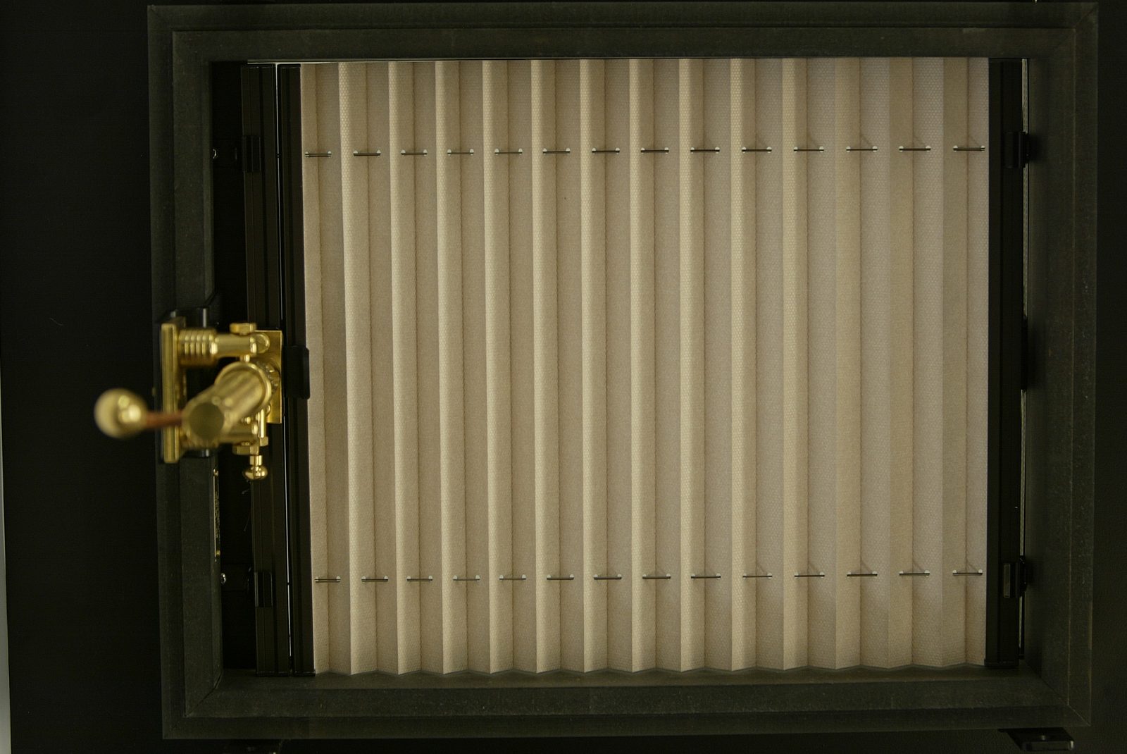 Brass screw-jack winder fixed to the frame of a rooflight fitted with a pleated blind, seen from inside