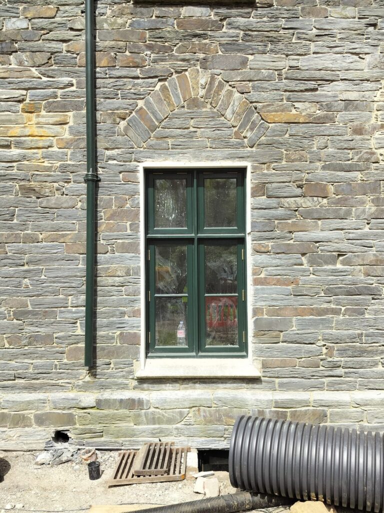 Cast iron gutter and downpipe on a slatestone house with a green painted window