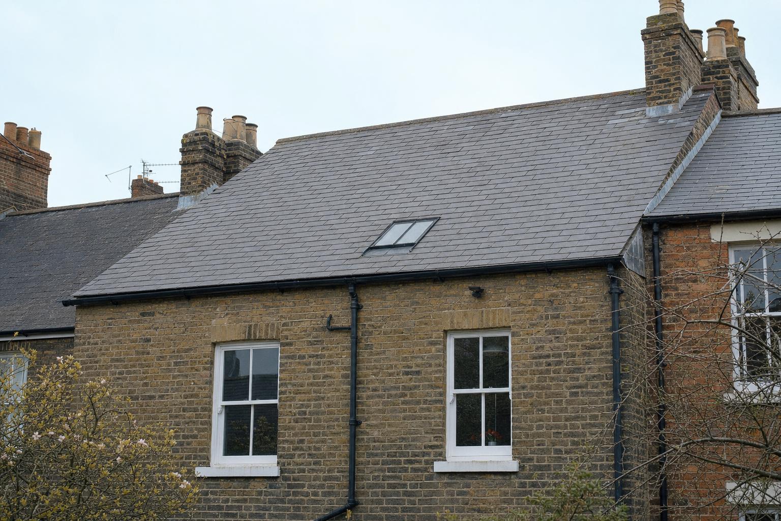 A single flush conservation rooflight on the rear slate roof slope of a terraced house, with cast iron gutter at the eaves.