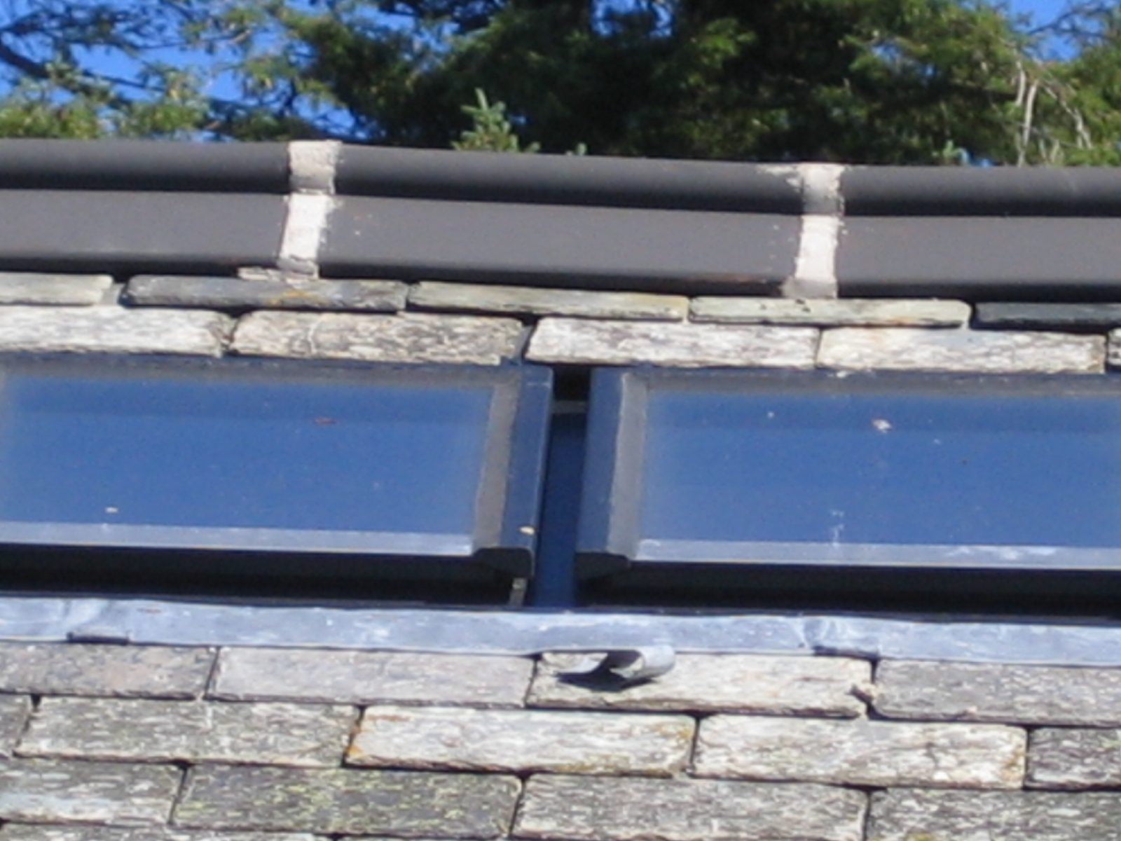 Detail of two conservation rooflight frames close to a ridge, showing the glazing, frame edge and the slate and lead junction