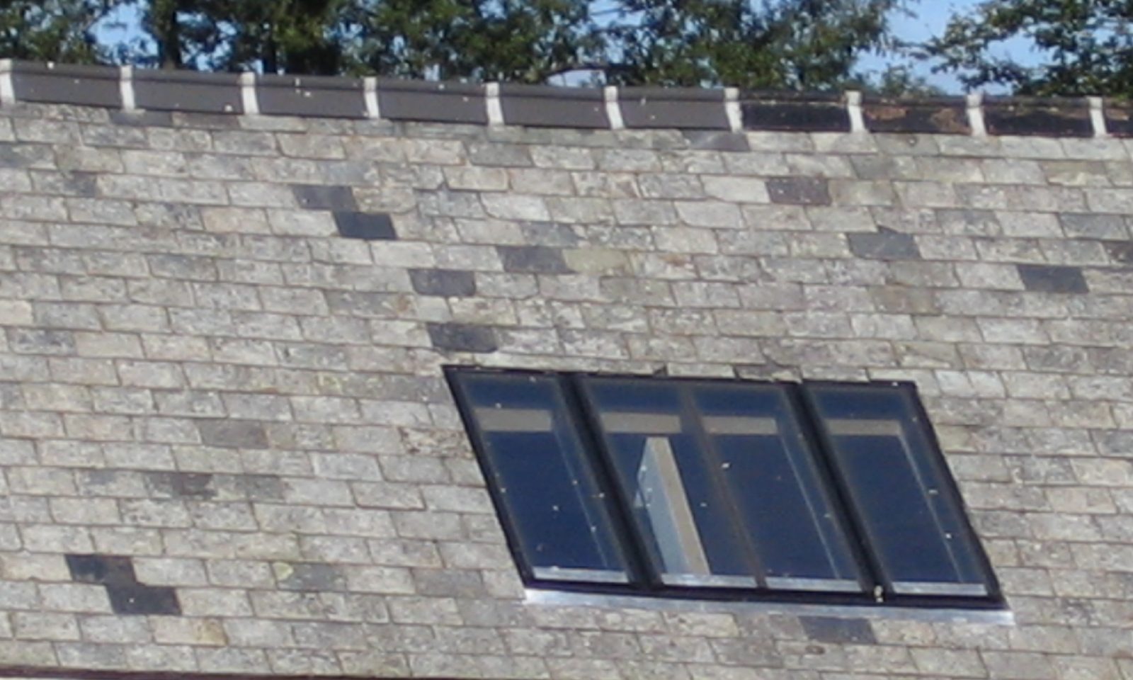 Conservation rooflight with glazing bars set into the weathered slate roof of a historic stable block below a clay-tile ridge