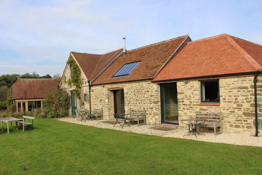 Stone barn conversion with a clay-tiled roof and a single linked conservation rooflight, black rainwater goods and a lawn in front