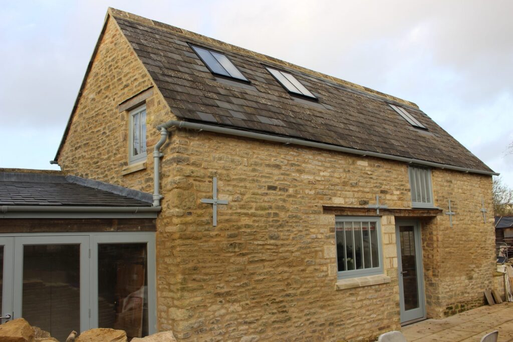 Three small conservation rooflights in the slate roof of a two-storey Bath stone cottage, painted rainwater goods at the eaves
