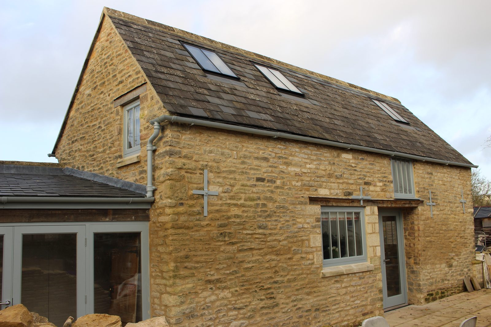 Three small conservation rooflights in the slate roof of a two-storey Bath stone cottage, painted rainwater goods at the eaves