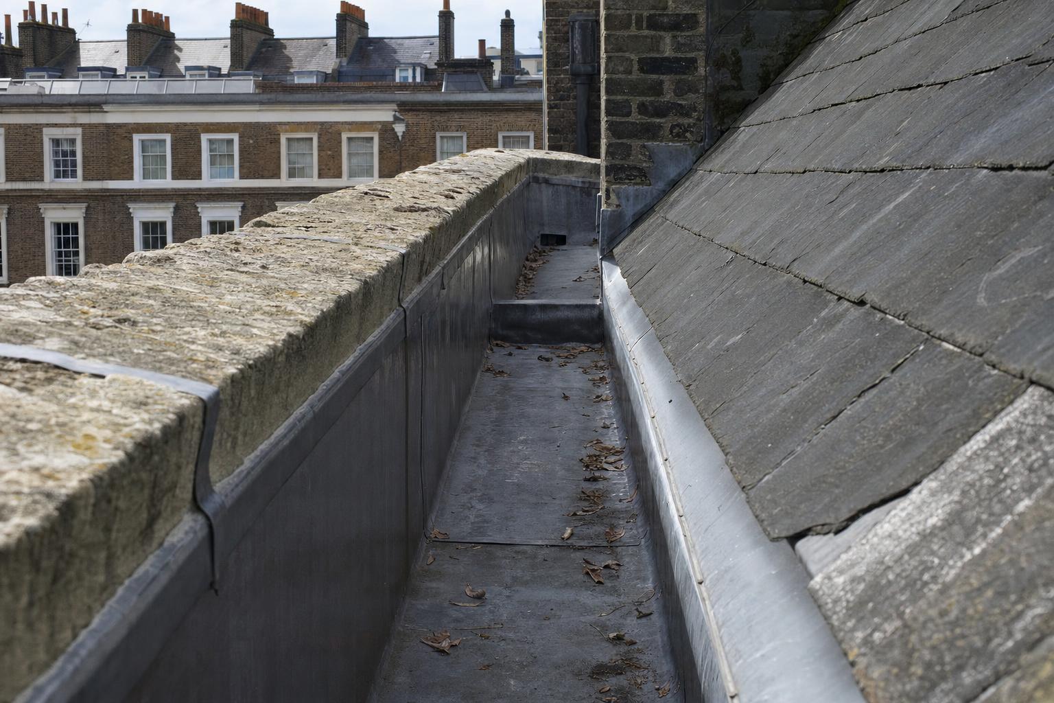 A lead-lined box gutter running behind a stone parapet on a Georgian roof, with a drip step and an outlet leading through the parapet.