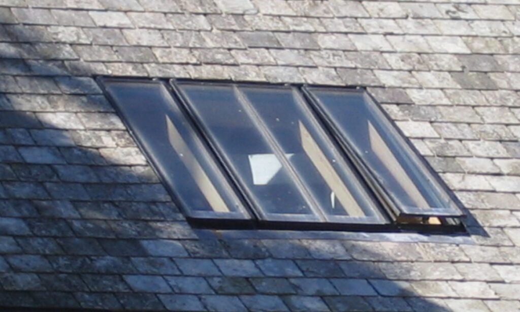 Linked conservation rooflight in a slate roof with its end sash slightly open and glazing bars over each pane