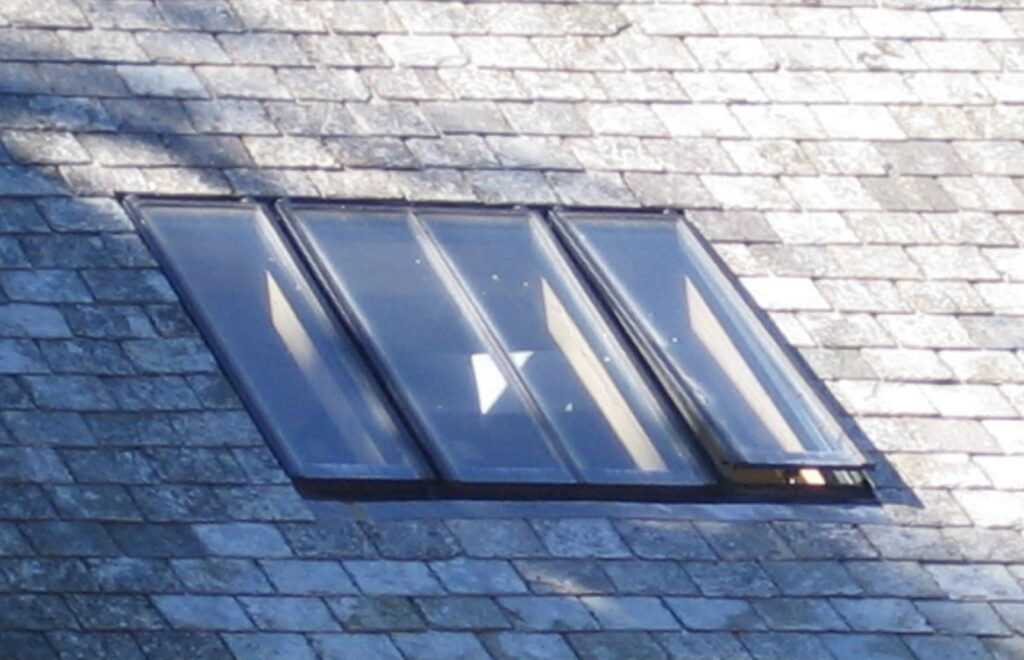 Three-bay linked conservation rooflight with slim glazing bars, fitted flush in a Devon slate roof with one sash open