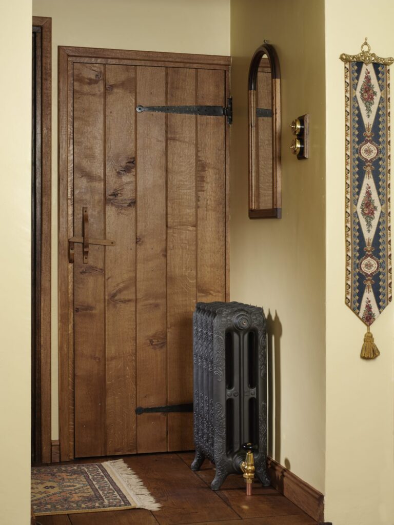 Compact Nouveau cast iron radiator beside a plank door on a cottage landing