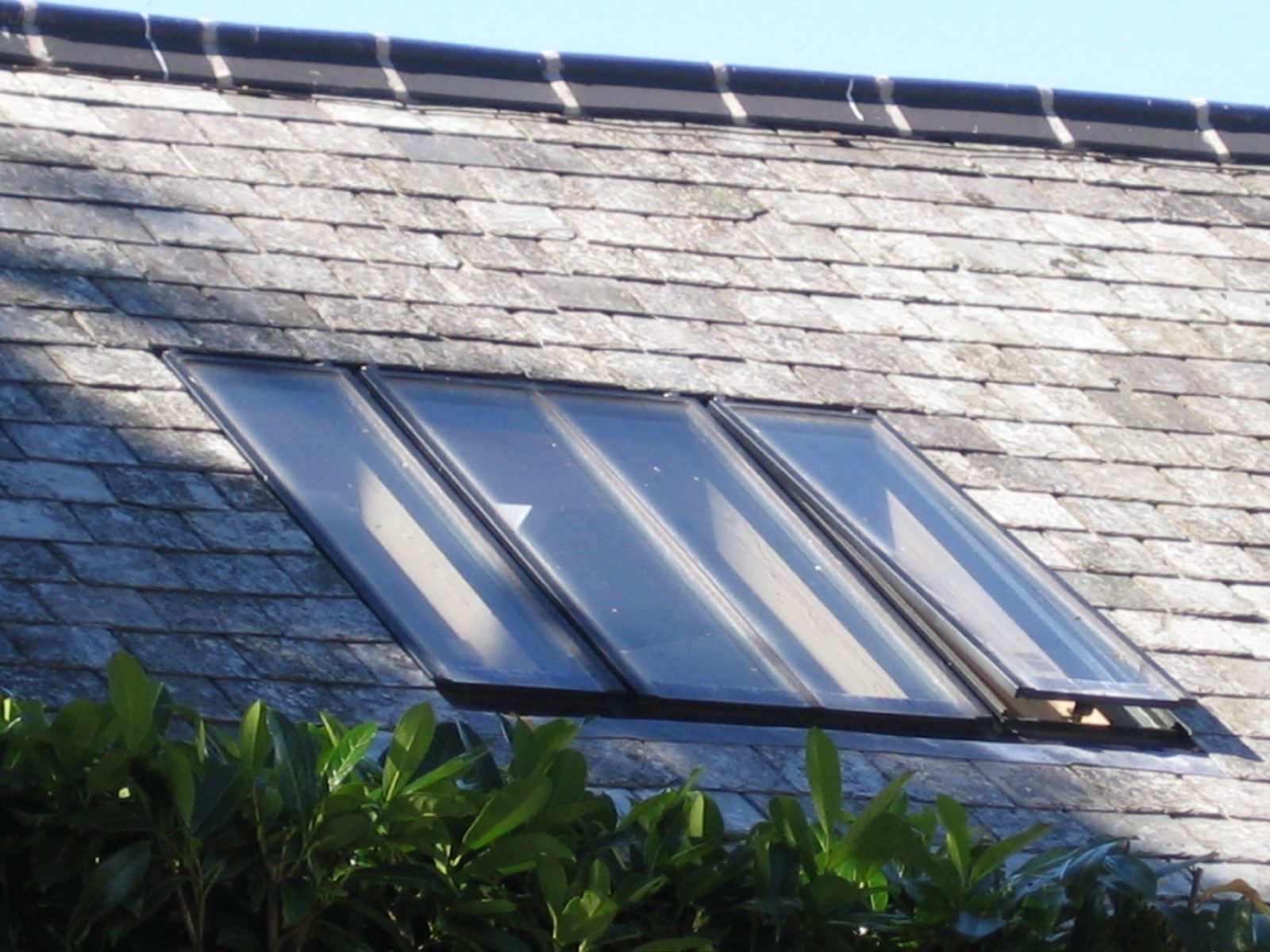 Close-up of a linked conservation rooflight in a slate roof below a clay ridge, with one top-hung sash partly open