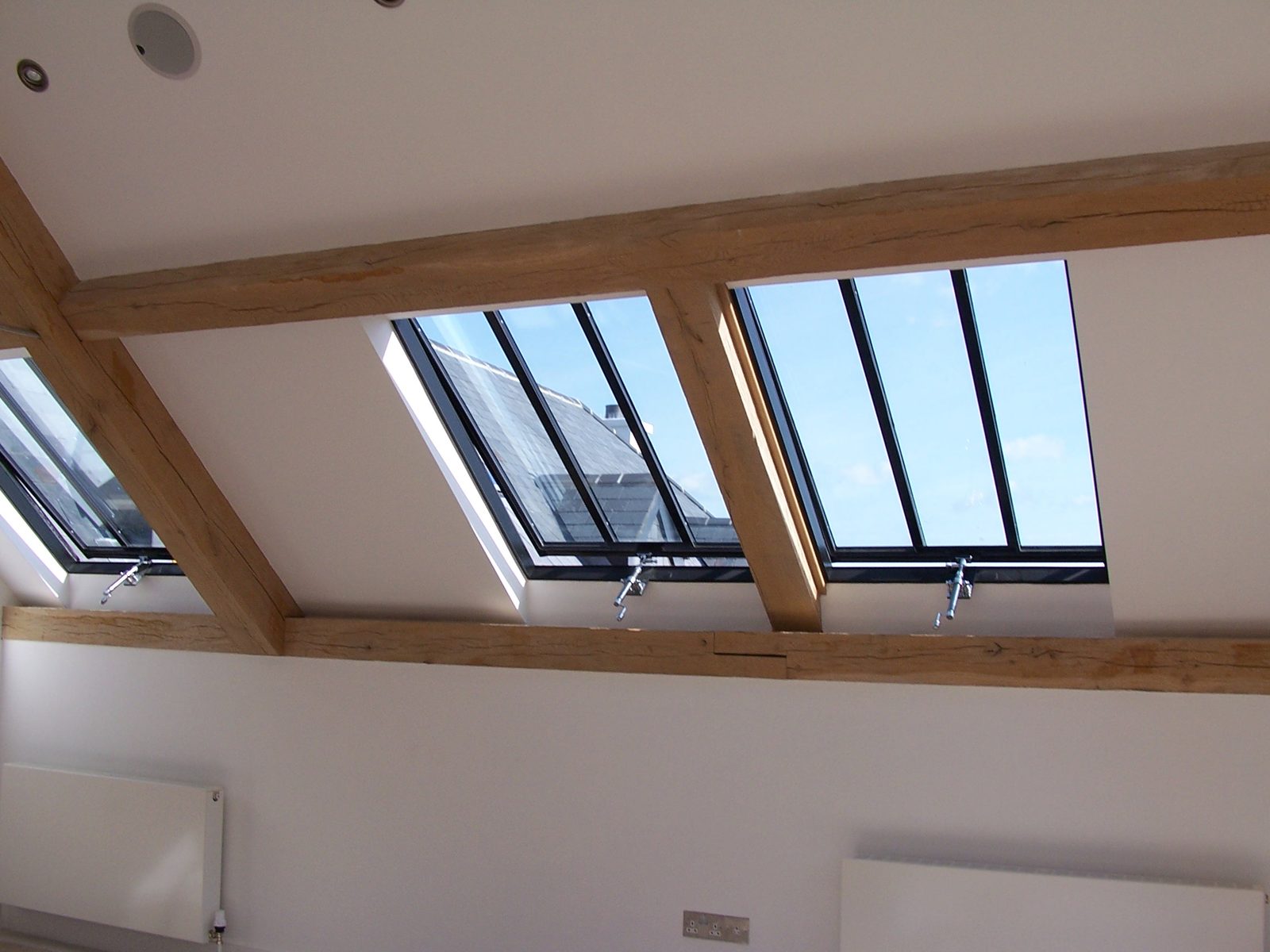 Interior with exposed oak beams and two opening rooflights with top-hung sashes propped open for ventilation