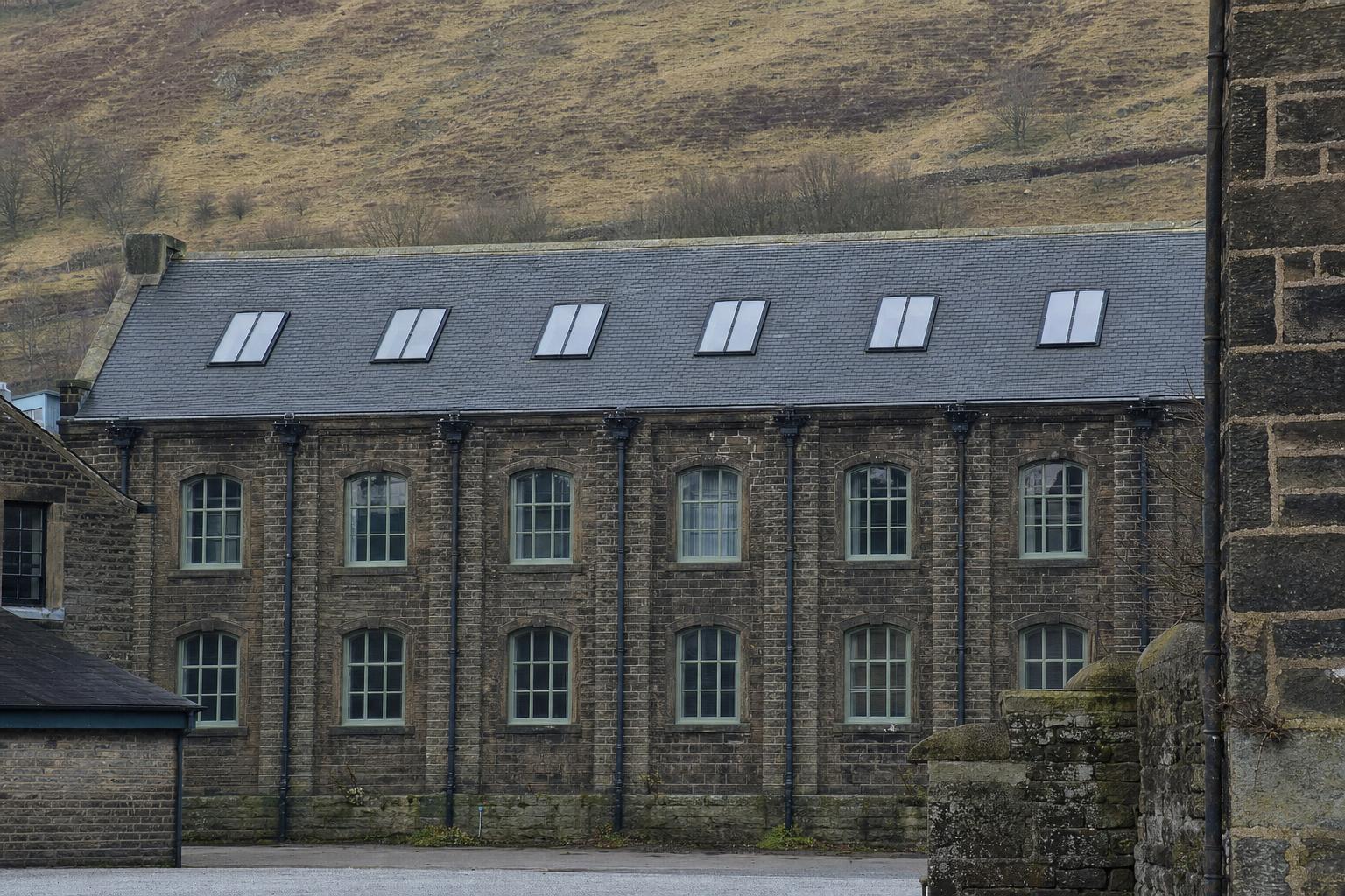 A long linked run of purpose-made heritage rooflights set flush into the slate roof of a converted nineteenth-century stone textile mill.