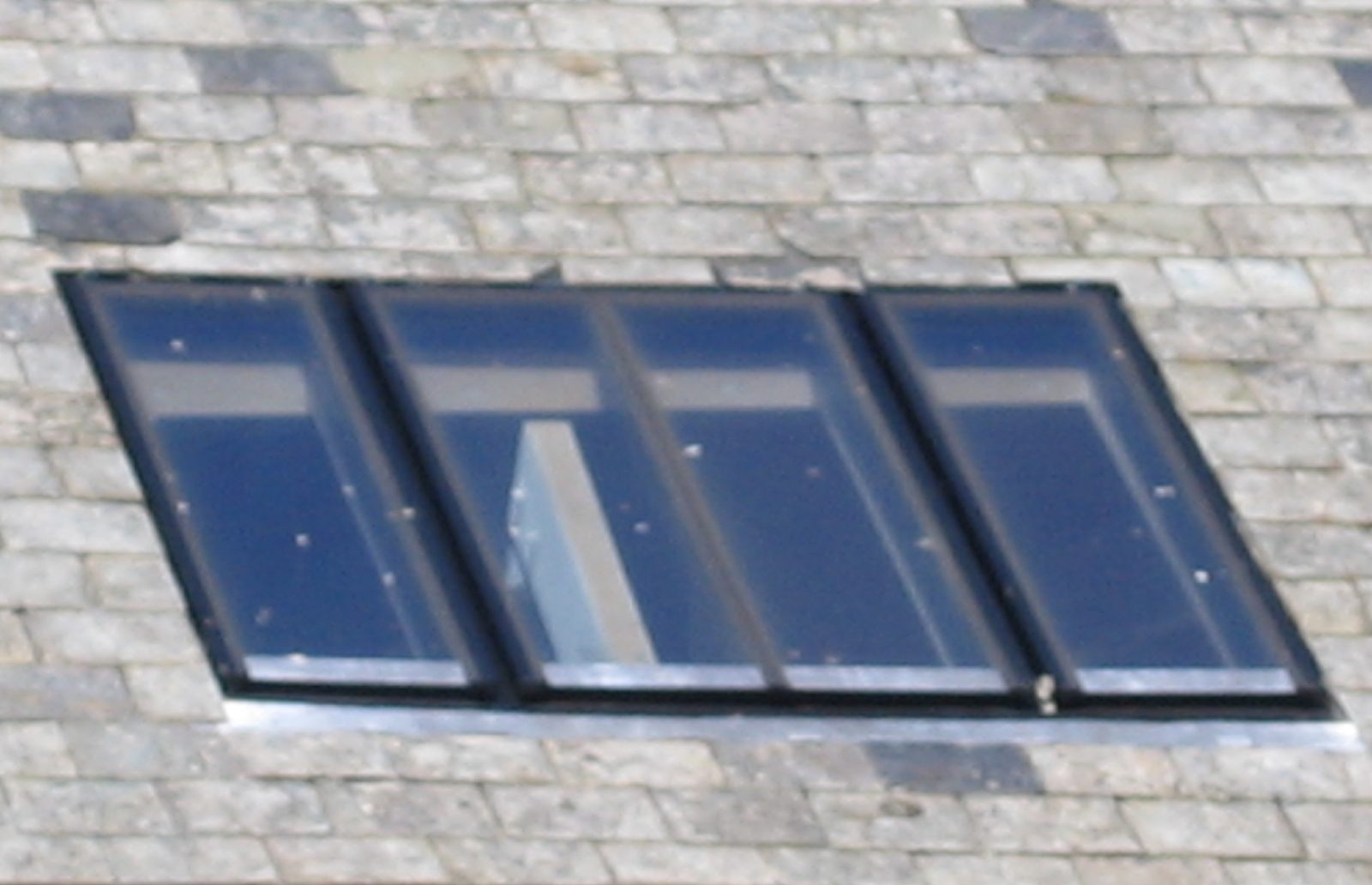 Close view of a three-bay conservation rooflight with black frames and narrow glazing bars sitting low in a slate roof
