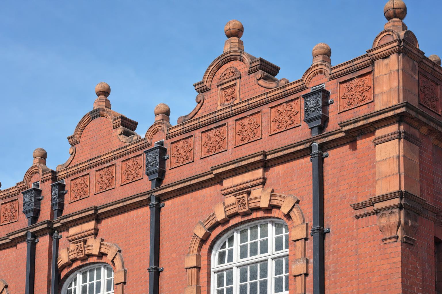 A red brick and terracotta Victorian public baths building with parapets, cast iron rainwater heads and downpipes.