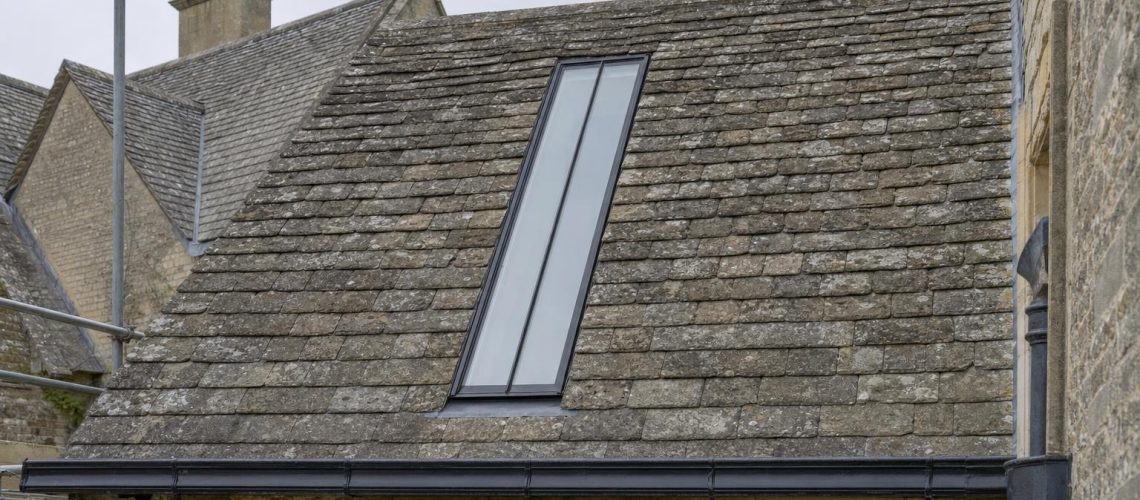 A long, narrow purpose-made conservation rooflight with a single central glazing bar set flush into the stone slate roof of a Georgian country house.