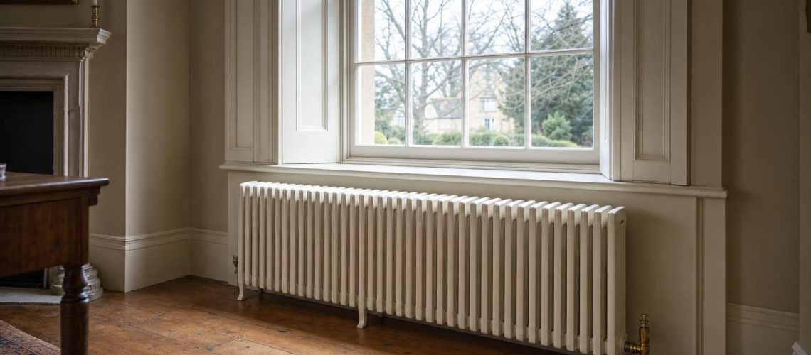 Cast iron column radiator beneath a tall sash window in a panelled Georgian room with brass angled valves.