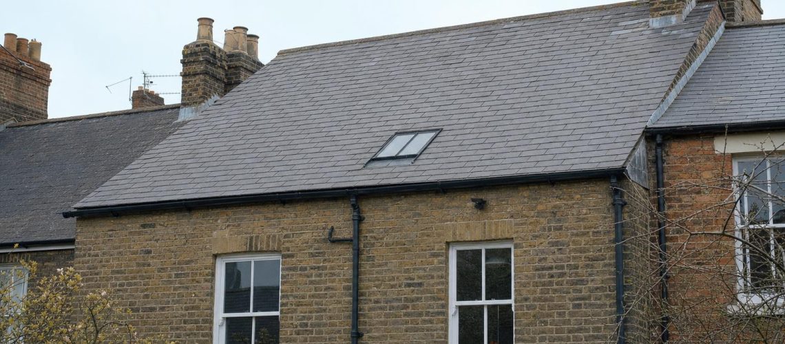 A single flush conservation rooflight on the rear slate roof slope of a terraced house, with cast iron gutter at the eaves.